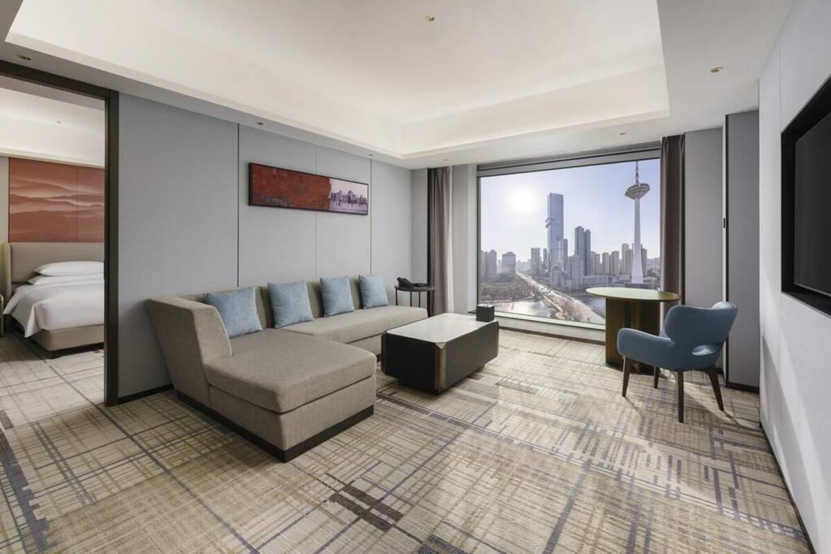 A modern hotel room with a large window, a sofa, a coffee table, and a chair.