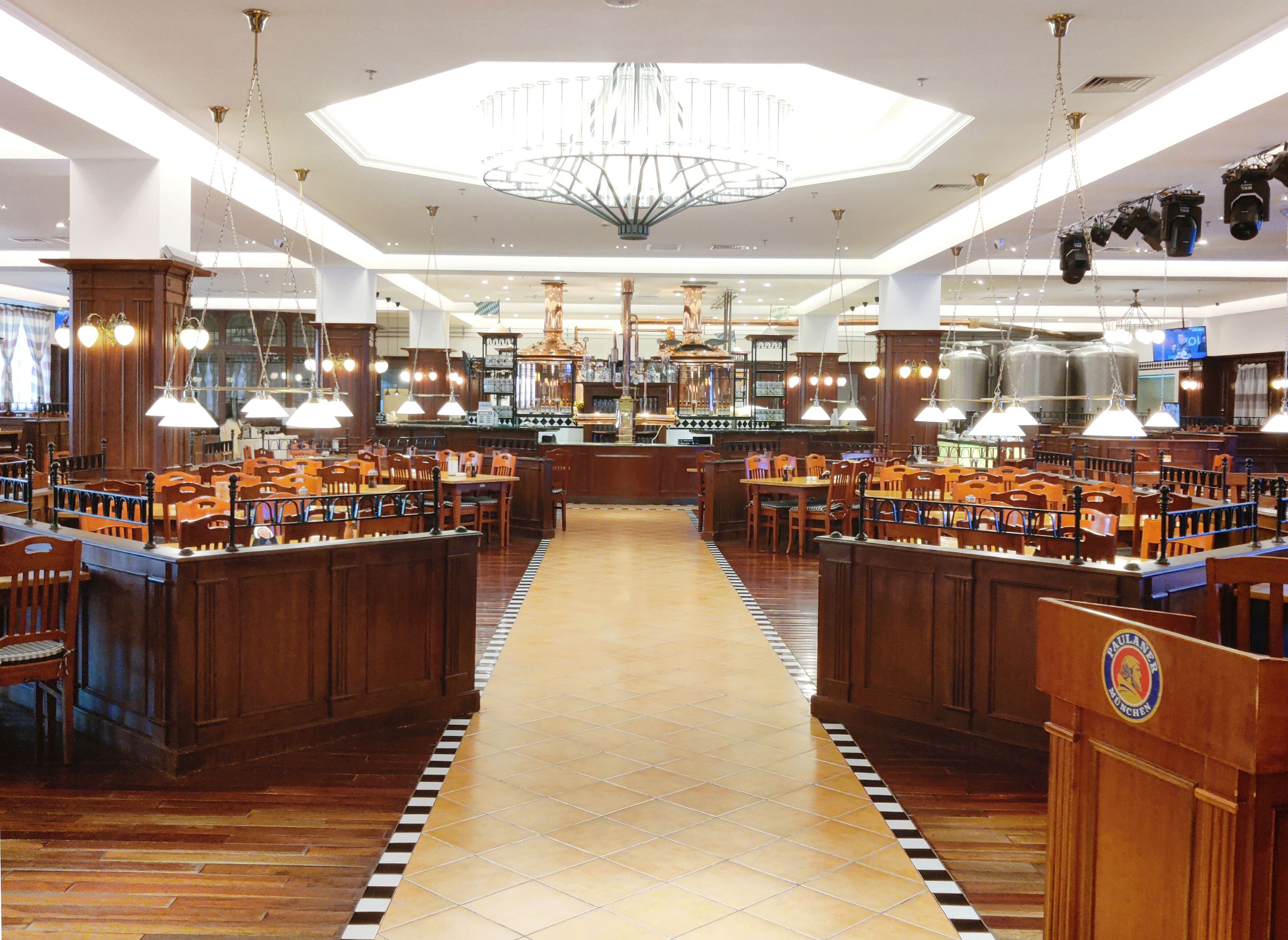 A spacious restaurant with wooden booths and tables, a central bar area, and a modern chandelier.