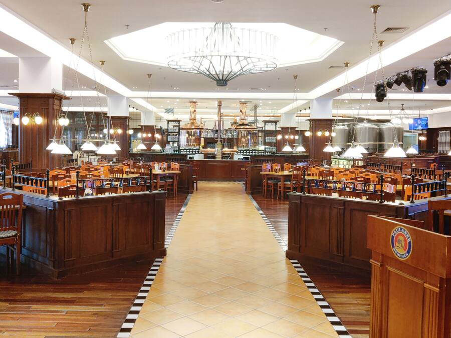 A spacious restaurant with wooden booths and tables, a central bar area, and a modern chandelier.