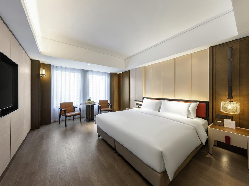A hotel room with a large bed, a desk, a chair, and a TV.