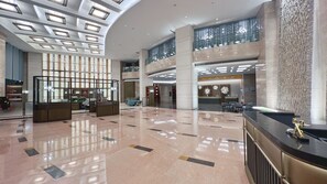 Un vestíbulo amplio con techo alto, una recepción, zona de estar y una escalera que sube a un nivel superior.