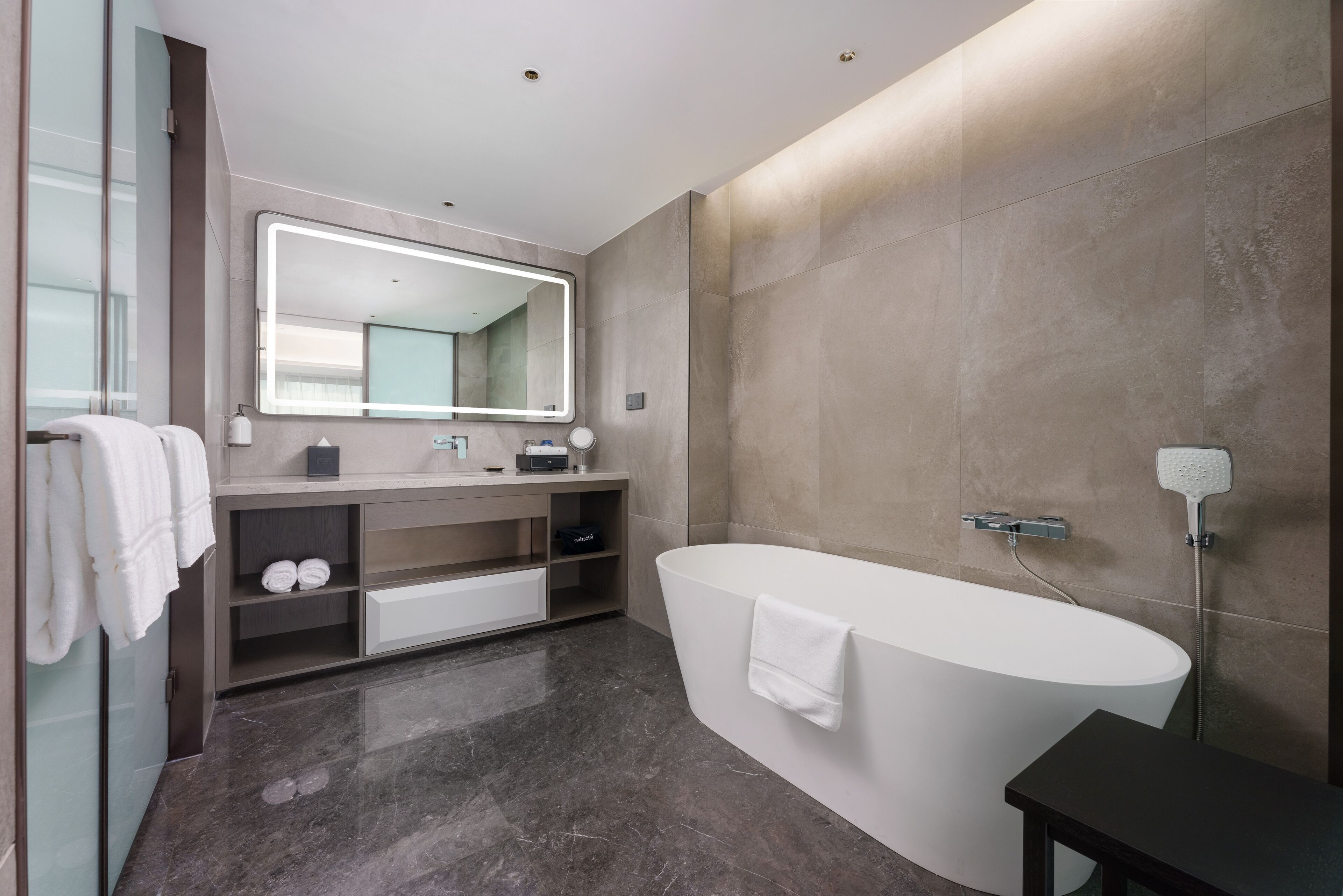 Un baño moderno con una bañera independiente, un espejo grande y un tocador con lavamanos y estantes.