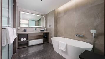 Un baño moderno con una bañera independiente, un espejo grande y un tocador con lavamanos y estantes.
