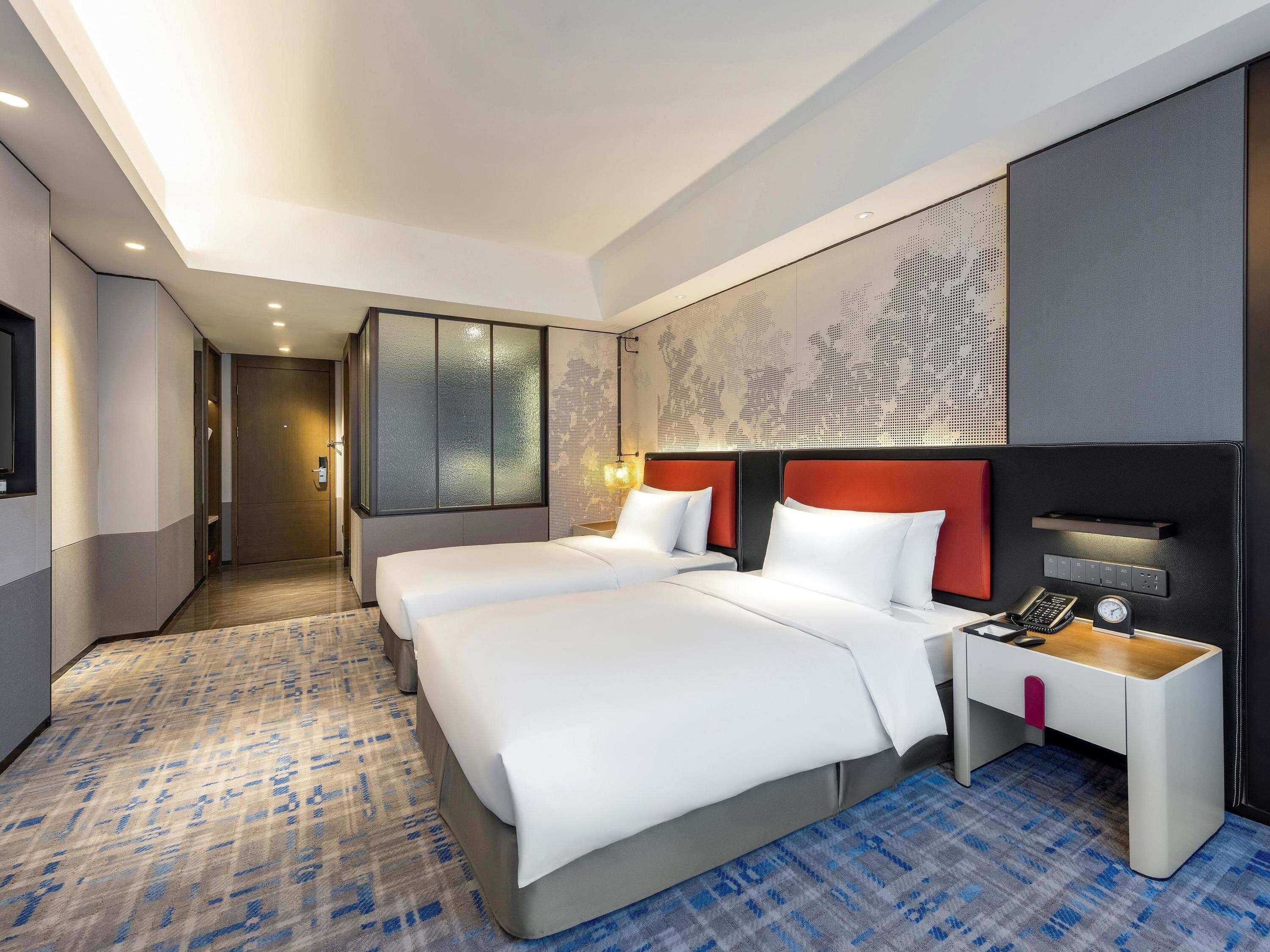 A hotel room with two beds, a desk, a phone, and a clock.