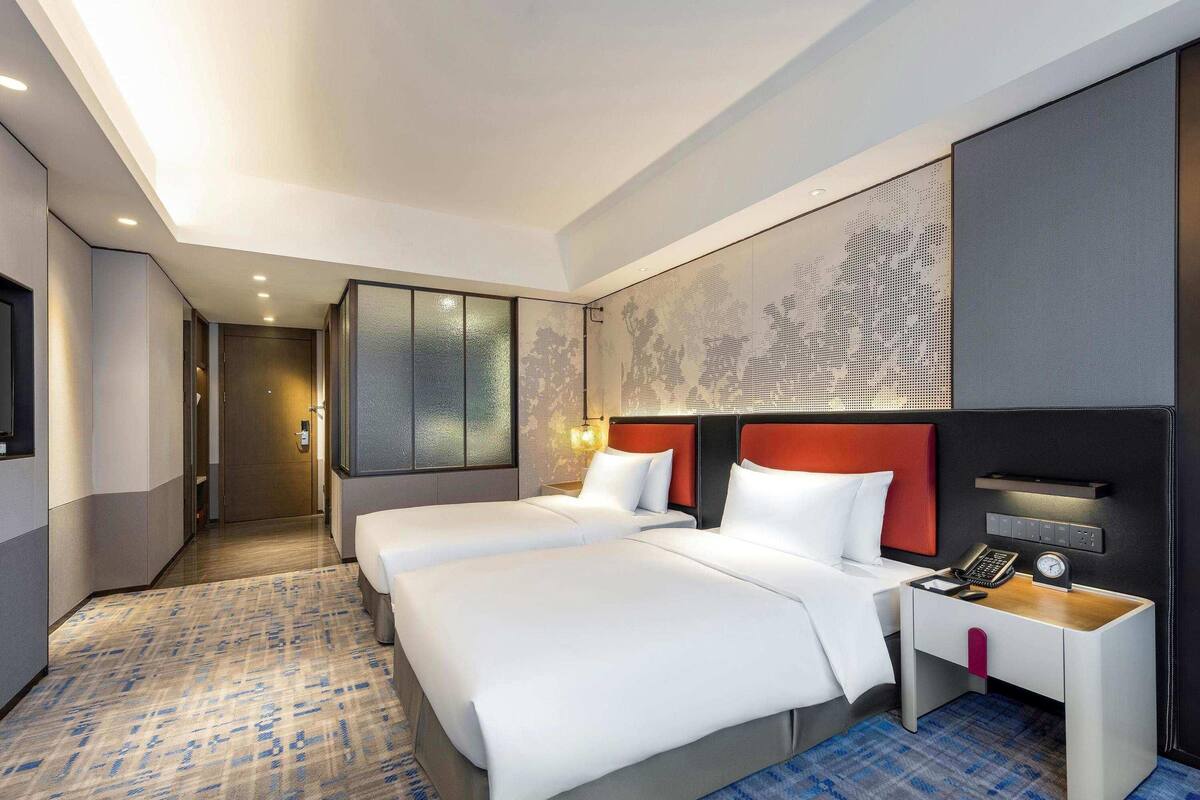 A hotel room with two beds, a desk, a phone, and a clock.