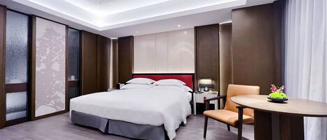 Habitación de hotel con cama, mesita de noche, silla y una pequeña mesa con un florero.