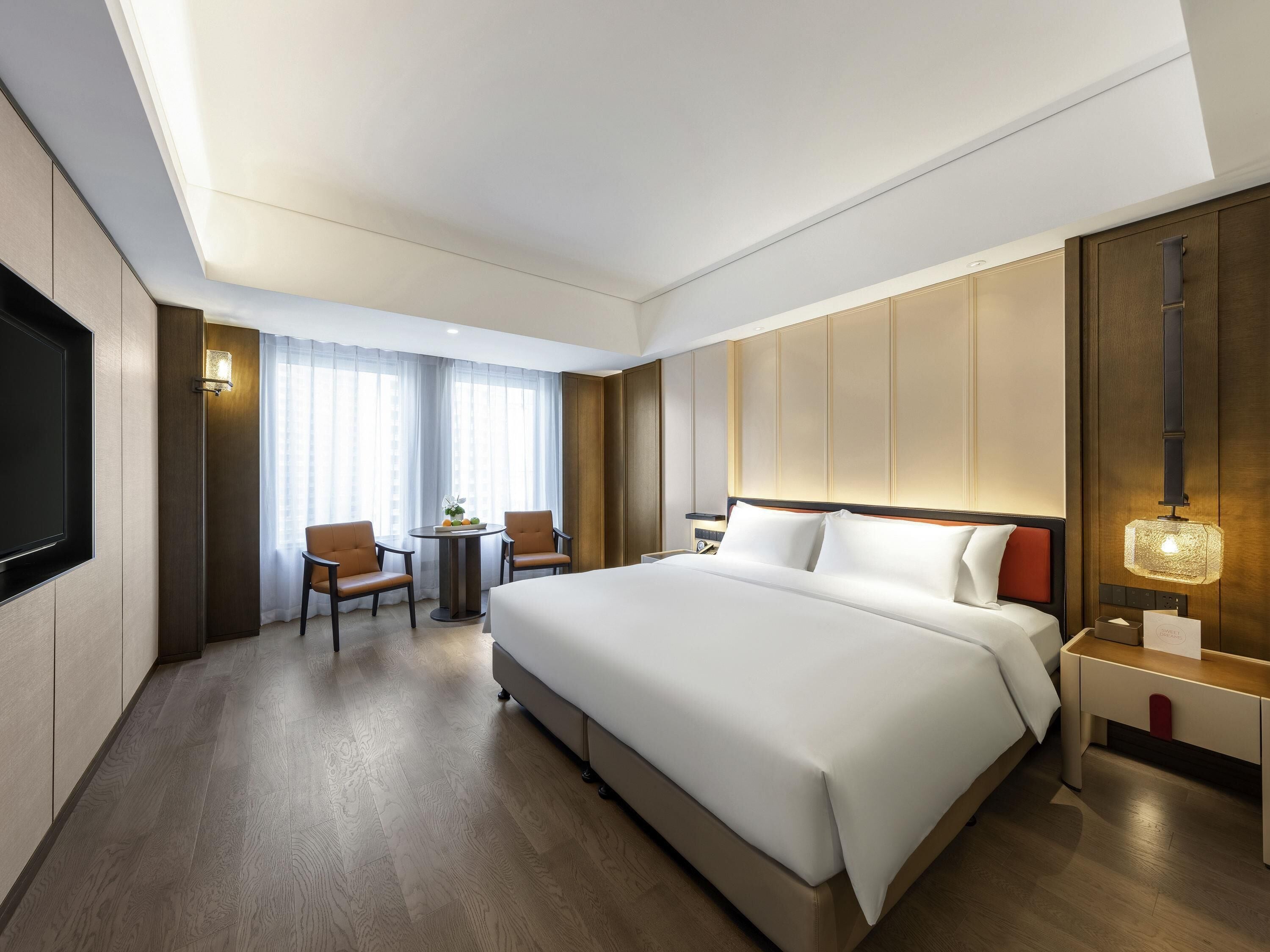 A hotel room with a large bed, a desk with a chair, a TV, and a window with curtains.