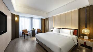 Quarto de hotel com uma cama grande, uma mesa com cadeira, televisão e janela com cortinas.