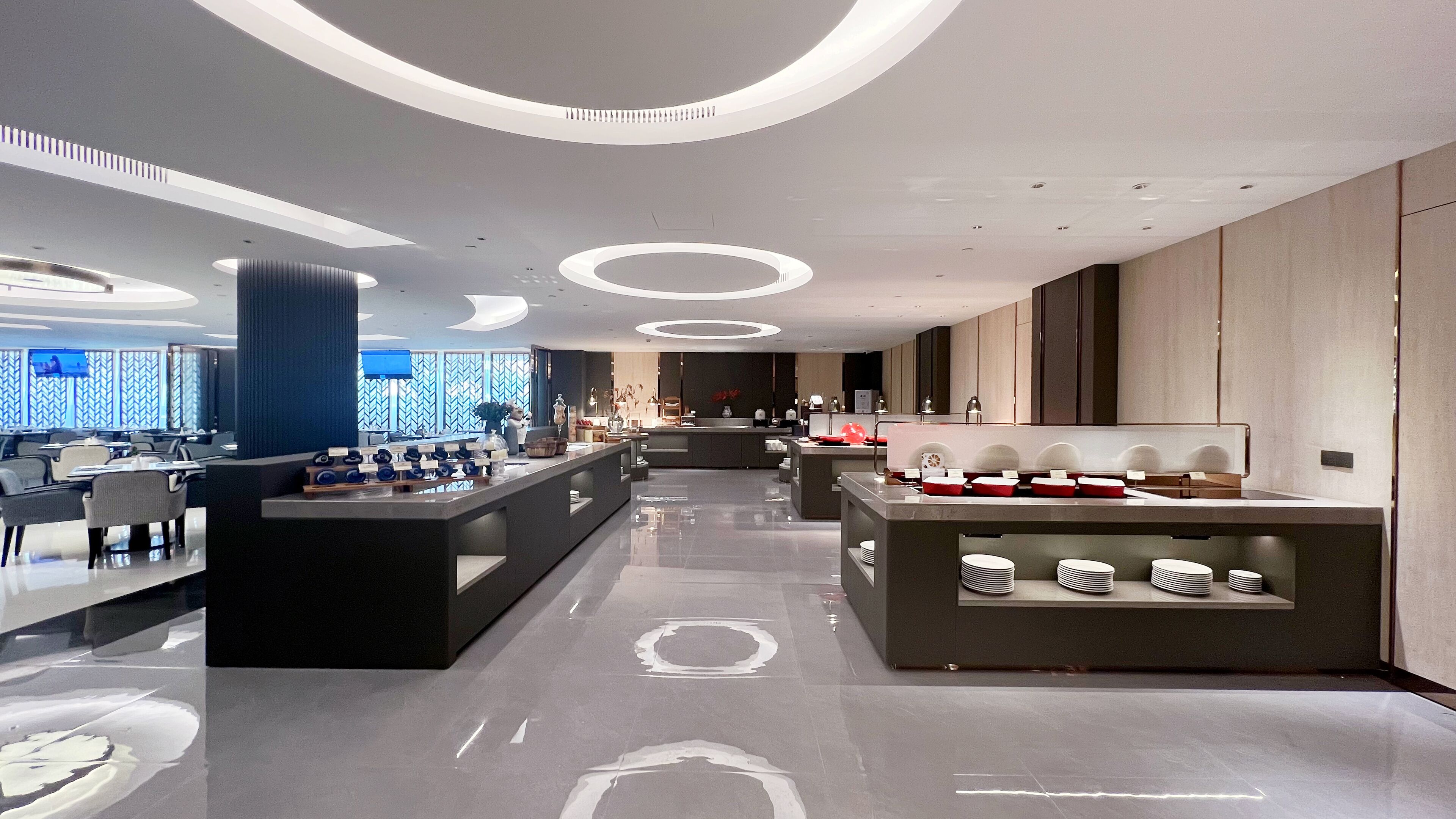 A modern hotel lobby with a central reception desk, seating area, and a large window with a view.