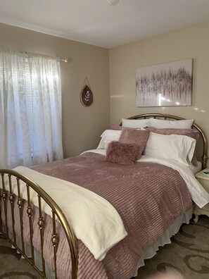 Une chambre à coucher avec un lit, des rideaux, une œuvre d’art accrochée au mur et une table de chevet.