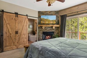 A bedroom with a large bed, a stone fireplace, a sliding barn door, and a view of trees through a window.