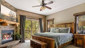 A bedroom with a fireplace, a bed, a bench, and a ceiling fan. - Eagle Creek Lodge w/Spa (Big Bear Lake)