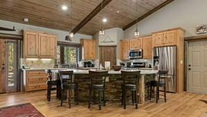 A spacious kitchen with wooden cabinets, a central island with bar stools, stainless steel appliances, and a rustic ceiling. - Eagle Creek Lodge w/Spa (Big Bear Lake)