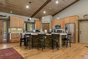 A spacious kitchen with wooden cabinets, a central island with bar stools, stainless steel appliances, and a rustic ceiling.