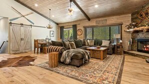 A rustic interior with a large sofa, a fireplace, wooden floors, and a dining area. - Eagle Creek Lodge w/Spa (Big Bear Lake)