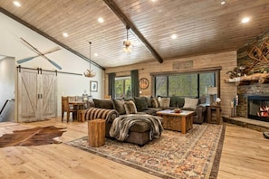A rustic interior with a large sofa, a fireplace, wooden floors, and a dining area.