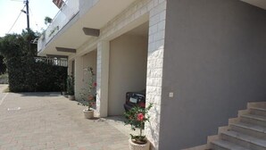 A building with a covered driveway, potted plants, and a staircase leading to the entrance.