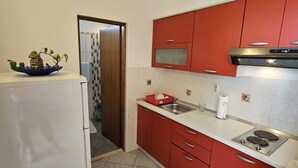 A compact kitchen with red cabinets, a white refrigerator, and a tiled backsplash.