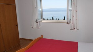 A room with a bed, a wooden wardrobe, and a window with a view of the sea.