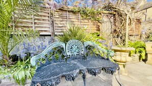 A wrought iron bench in a garden setting with a stone wall and flowering plants. - The Kyrenia (Weston-super-Mare)