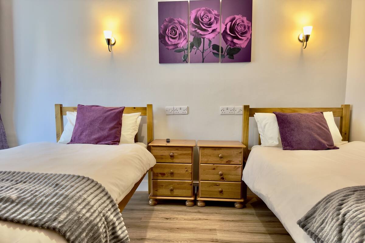 A double room with two beds, each with a wooden headboard, a nightstand with drawers, and a wall-mounted light fixture.