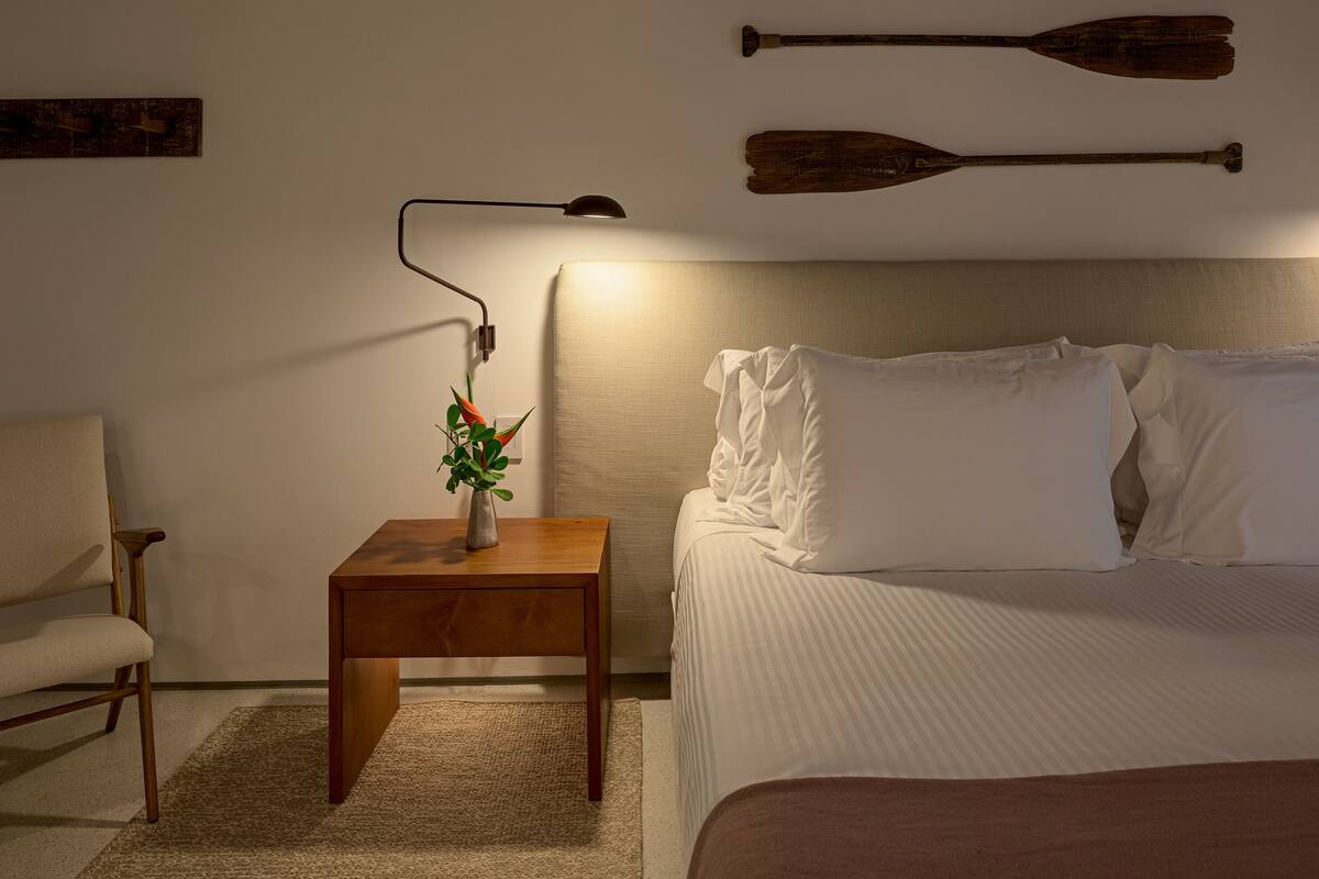 A neatly arranged bedroom with a bed, bedside table, lamp, and a wall-mounted paddle.