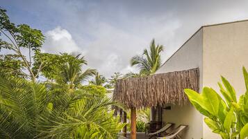A tropical resort with a thatched-roof structure, wooden deck, and lush greenery.