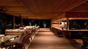 A spacious indoor area with wooden flooring, a long bench seating area, and a bar counter with stools.