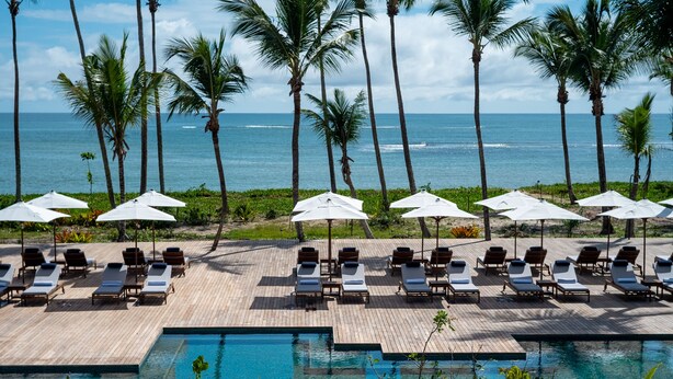 A poolside area with lounge chairs and umbrellas, overlooking the ocean.