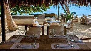 A beachside dining area with tables set for two, overlooking the ocean.