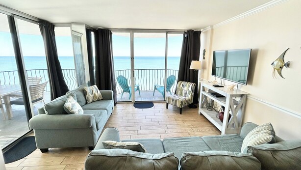 Ett vardagsrum med en soffa, fåtöljer, en tv och utsikt över havet.
