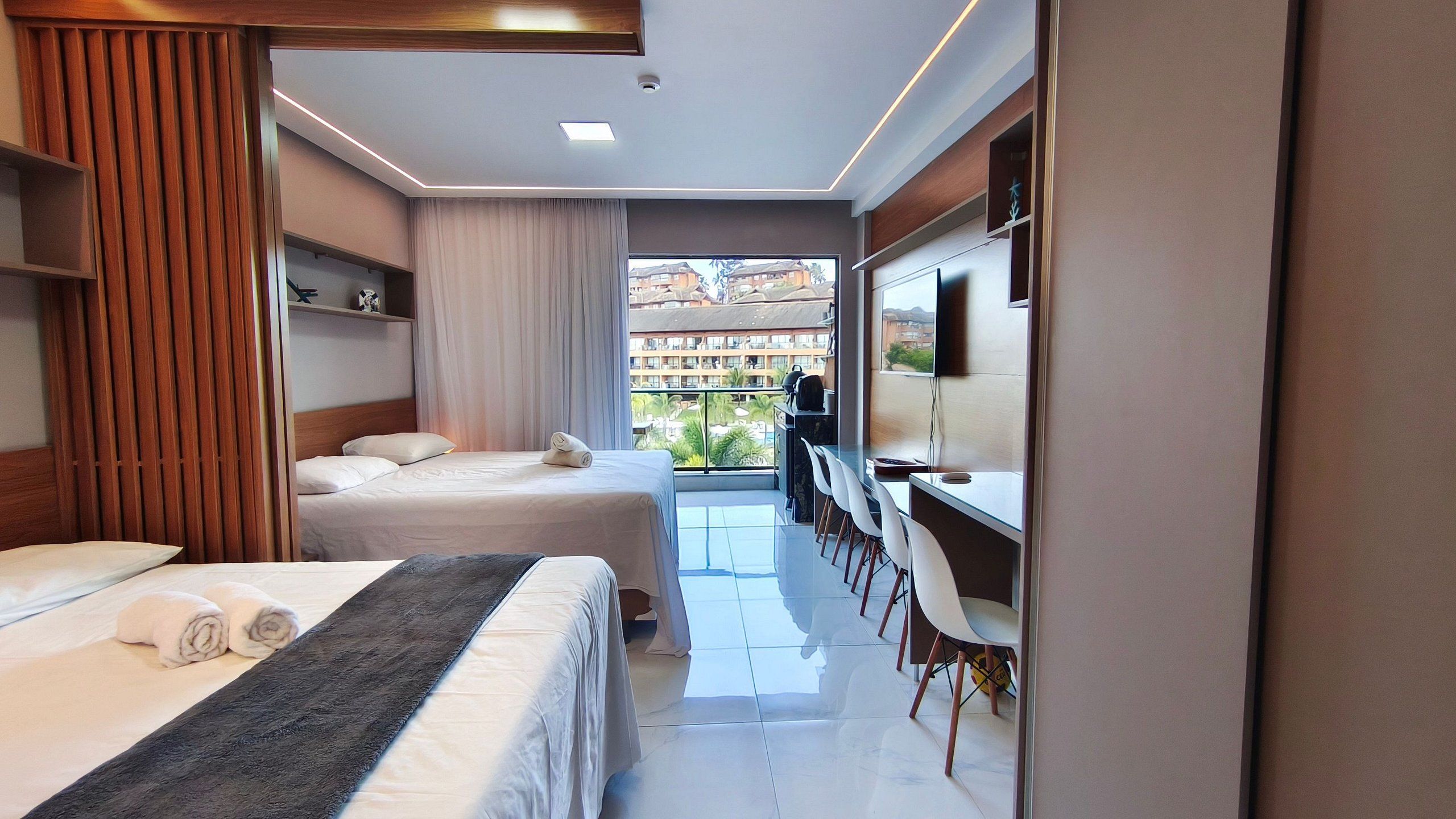 Een hotelkamer met twee bedden, een bureau, een televisie en een balkon met uitzicht op gebouwen.