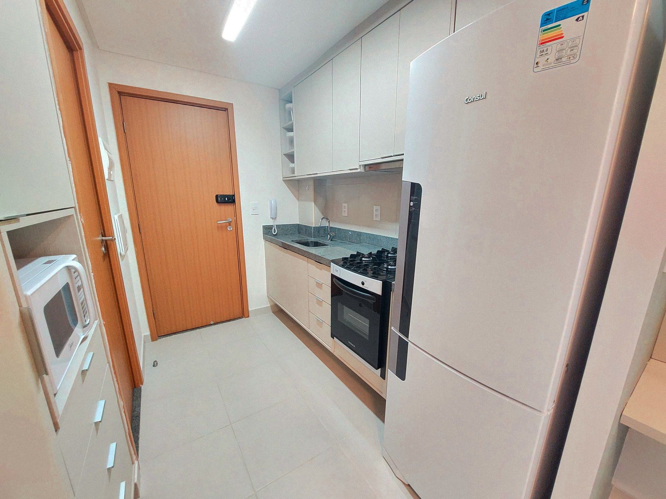 A compact kitchen with a refrigerator, stove, microwave, and a wooden door.