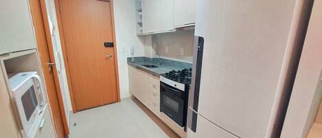 A compact kitchen with a refrigerator, stove, microwave, and a wooden door.