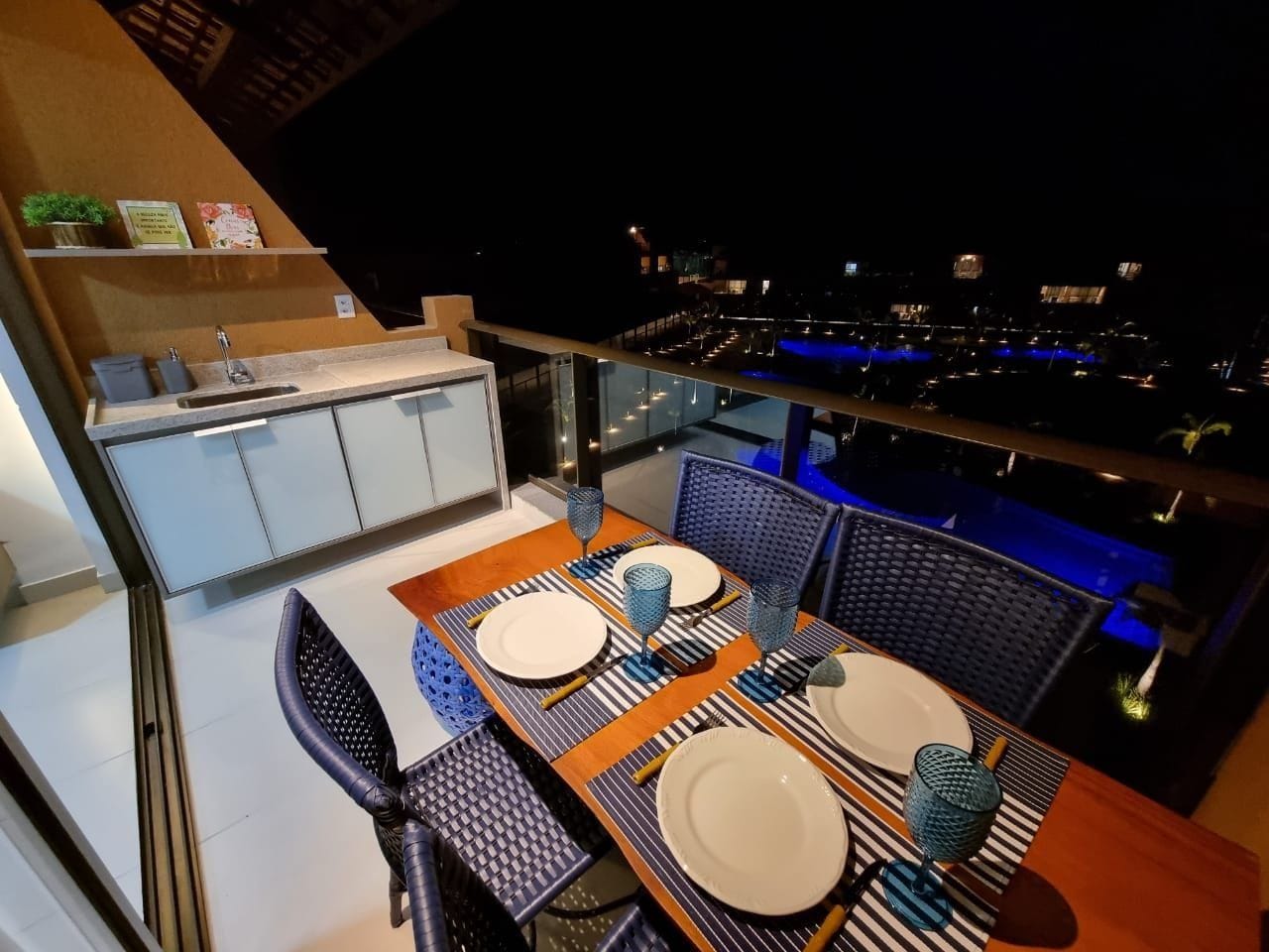 A dining area with a table set for two, a kitchen area, and a view of the city at night.
