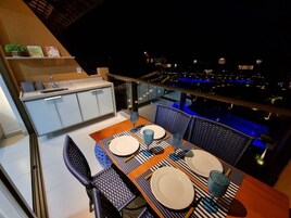 Un comedor con una mesa dispuesta para dos, una zona de cocina y vistas a la ciudad de noche.