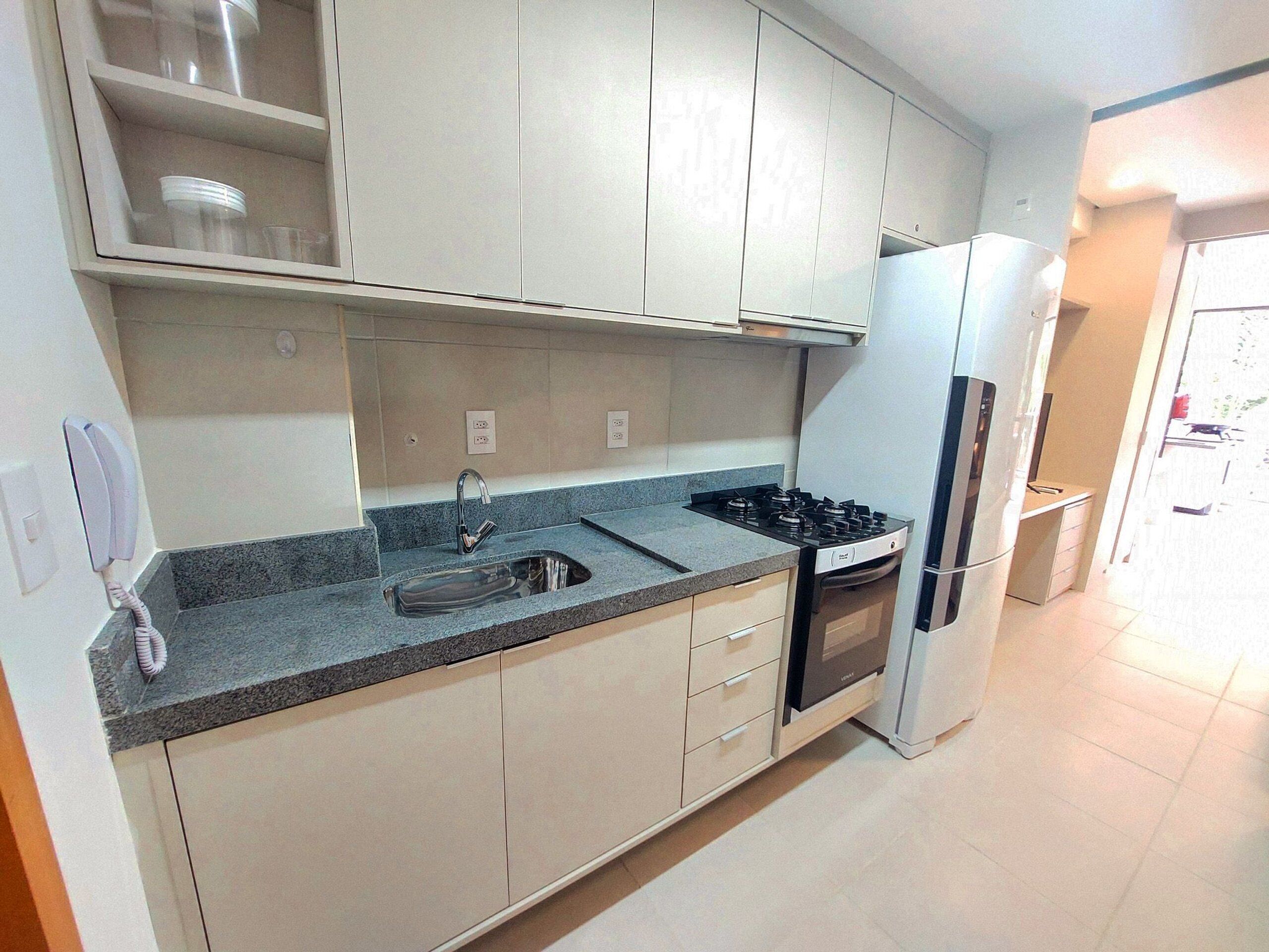 A kitchen with a sink, stove, and refrigerator, with cabinets above and a phone on the wall.