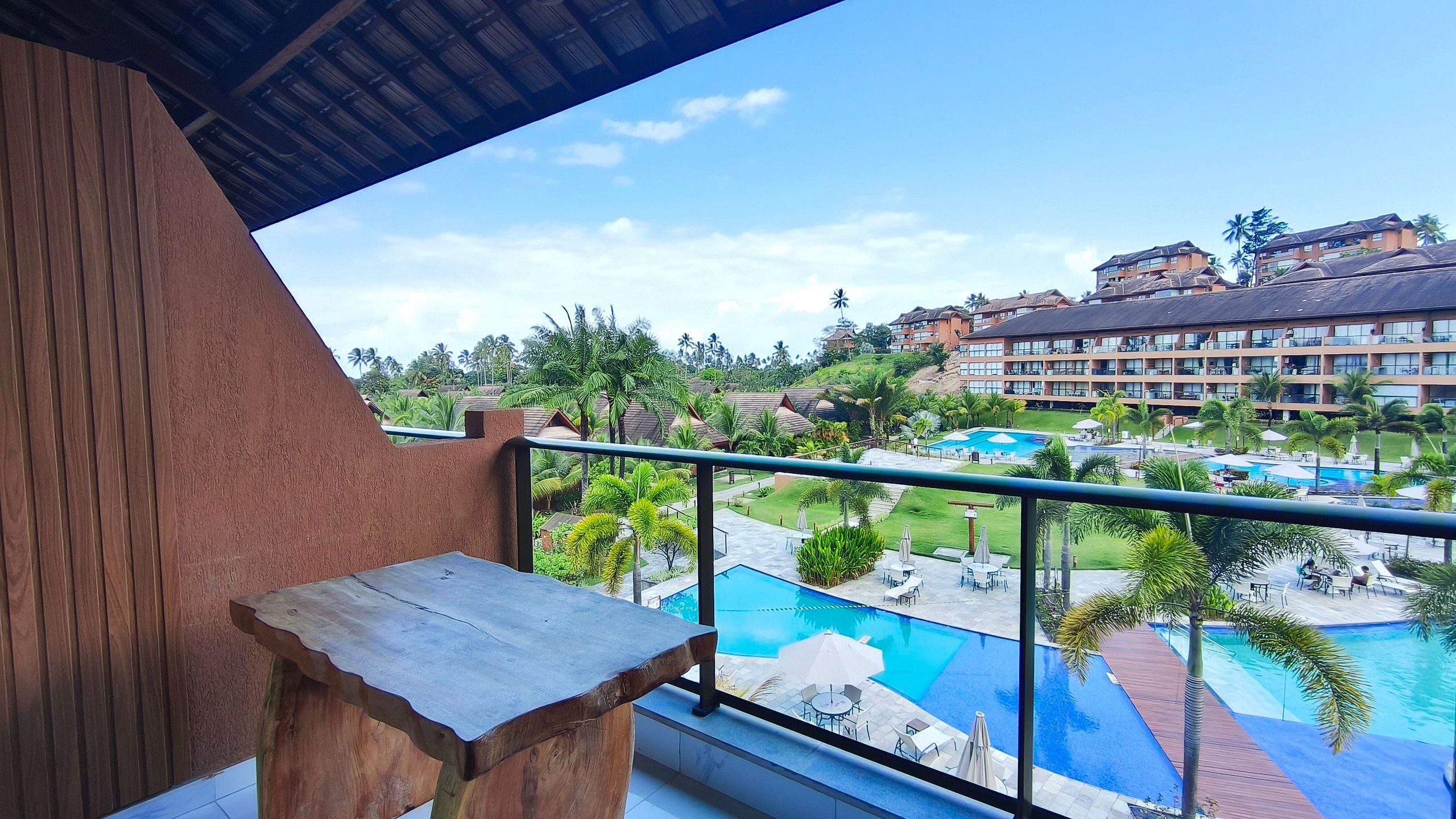 Ein Balkon mit Holztisch, mit Blick auf einen Swimmingpool und Hotelgebäudekomplex.