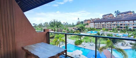 Ein Balkon mit Holztisch, mit Blick auf einen Swimmingpool und Hotelgebäudekomplex.