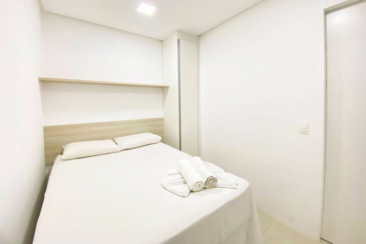 Una habitación de hotel moderna con cama, cabecero de madera, pared blanca y una puerta.