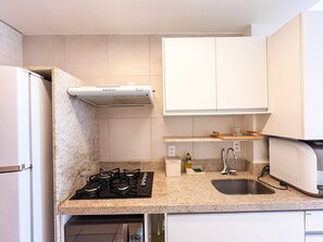 Una cocina con estufa a gas, horno empotrado, microondas, pileta y un armario blanco sobre la encimera.