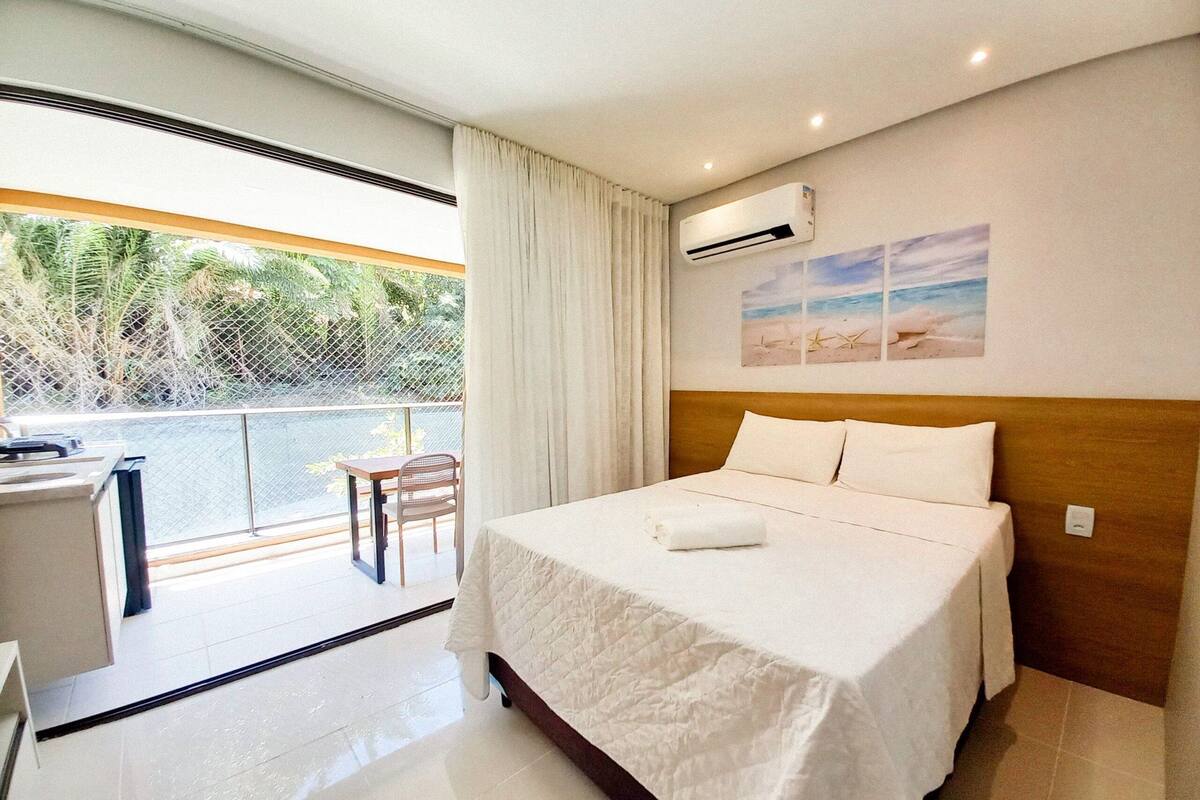 Habitación de hotel con cama, escritorio, silla, balcón y vistas a la vegetación, además de un aire acondicionado.