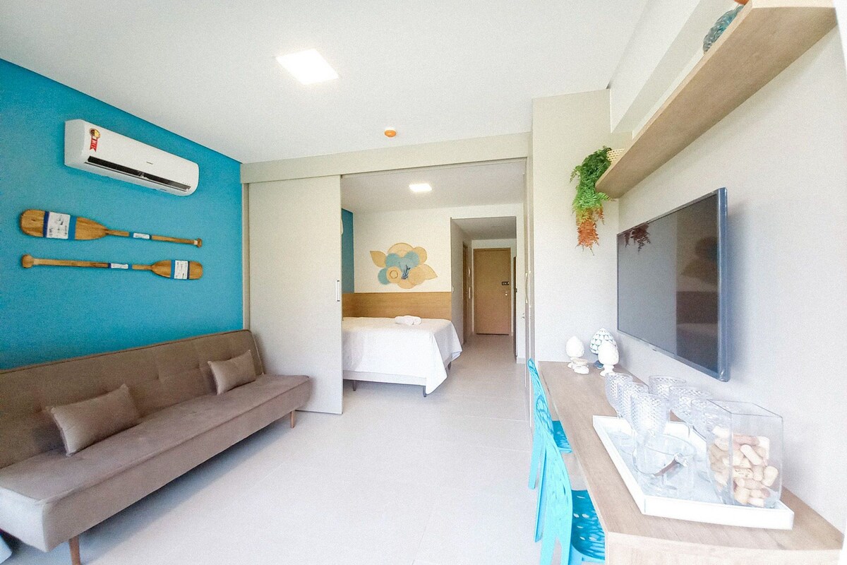 A hotel room with a sofa, a bed, a TV, and a wall-mounted air conditioner.