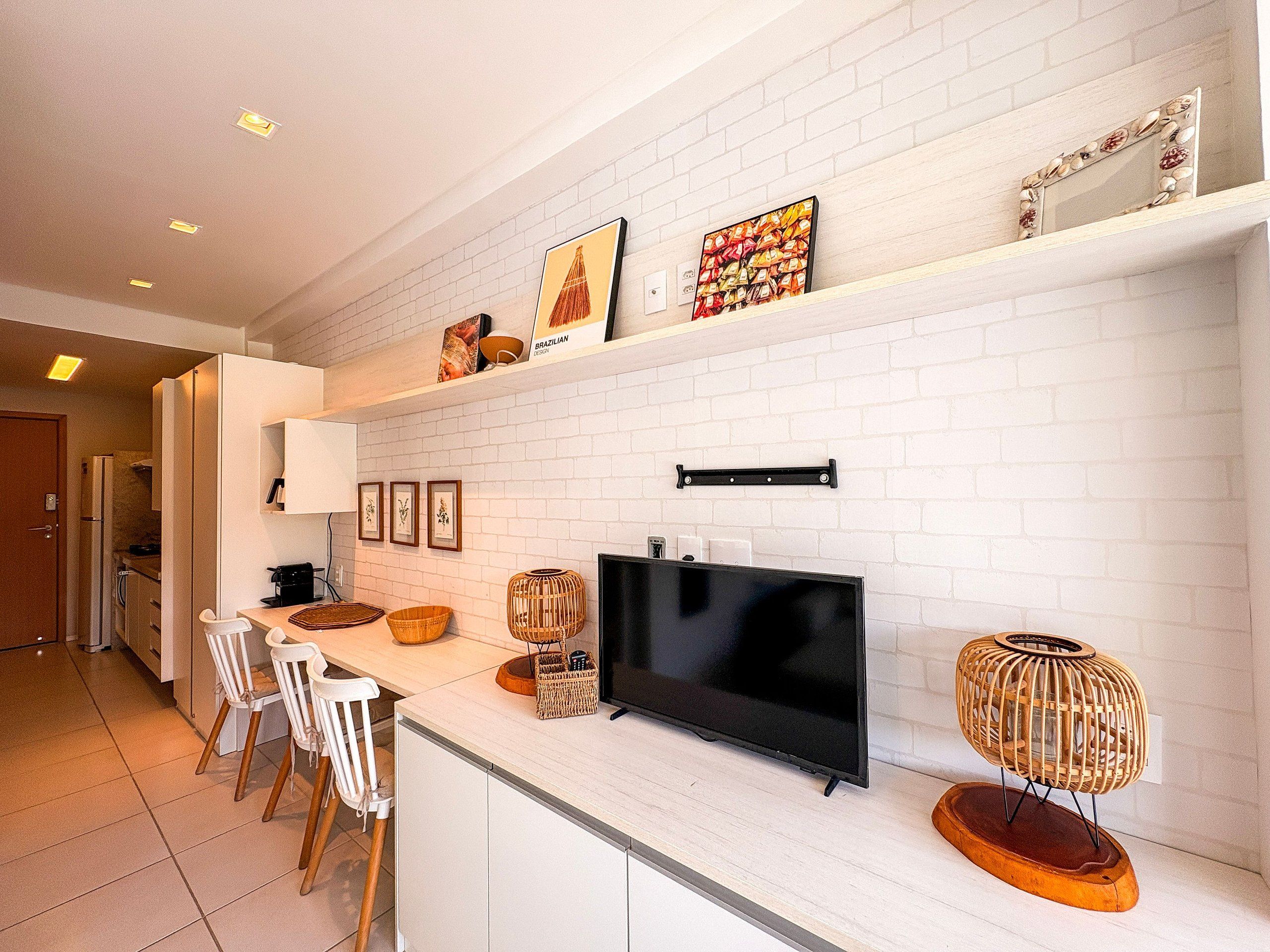 Une cuisine moderne avec des murs en briques blanches, un téléviseur à écran plat et un coin repas avec des chaises blanches.