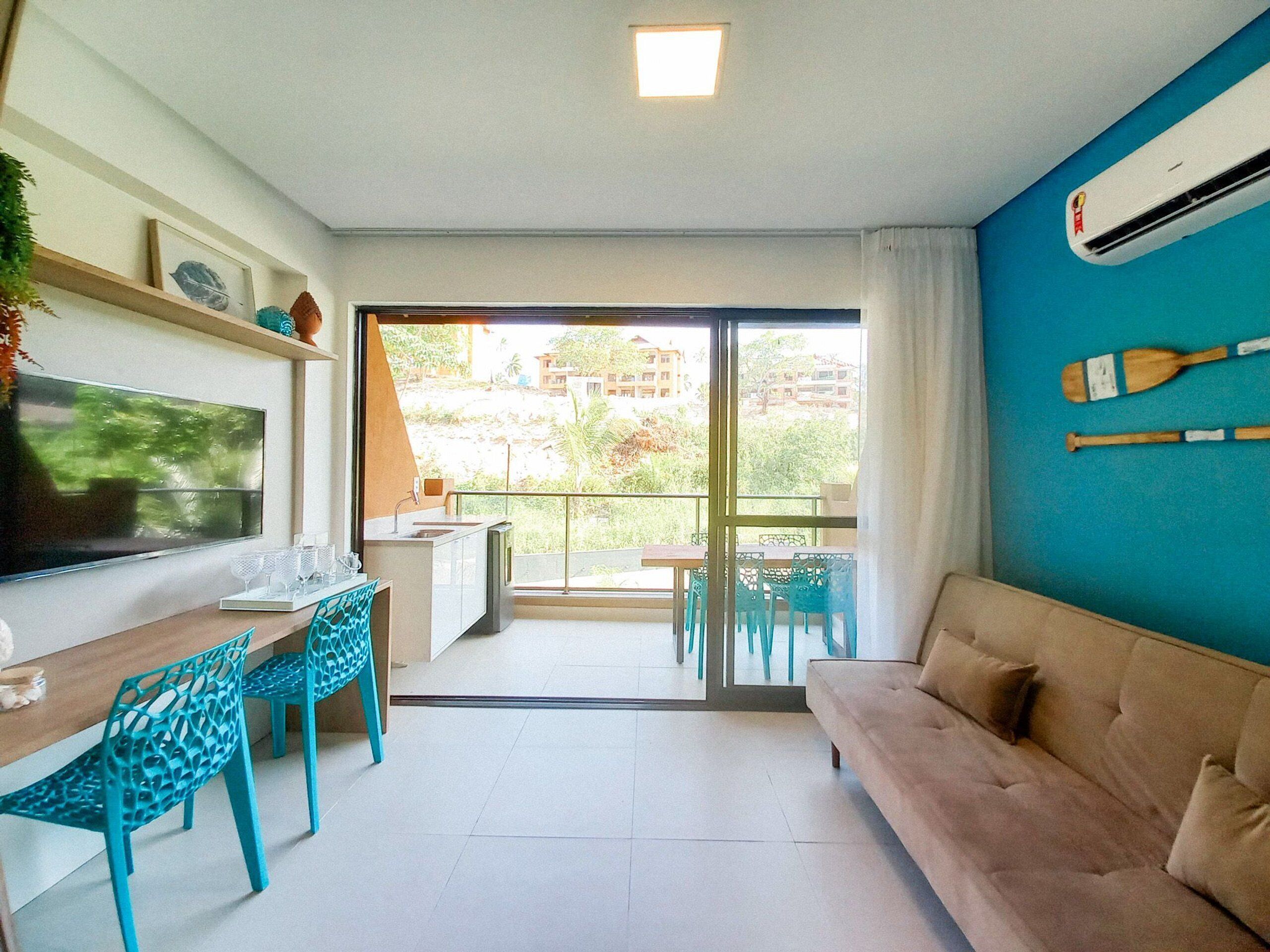 A modern living room with a sofa, a TV, a dining area with chairs, and a balcony with a view.