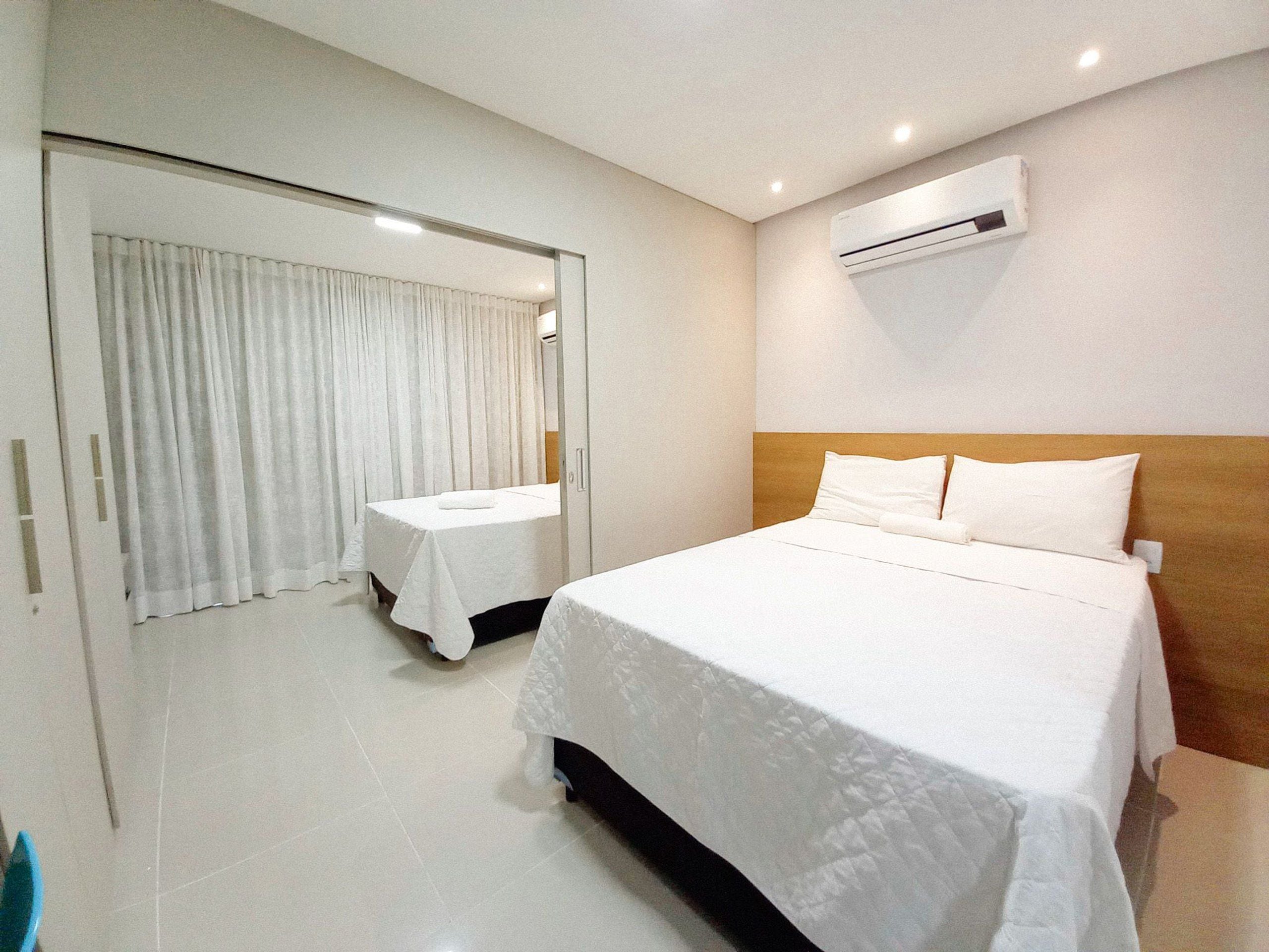 Habitación de hotel con una cama grande, una cama más pequeña, un espejo, un equipo de aire acondicionado y una puerta con cortinas.