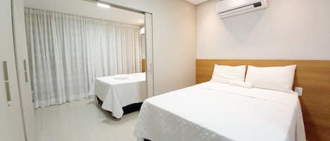 A hotel room with a large bed, a smaller bed, a mirror, an air conditioning unit, and a door with curtains.