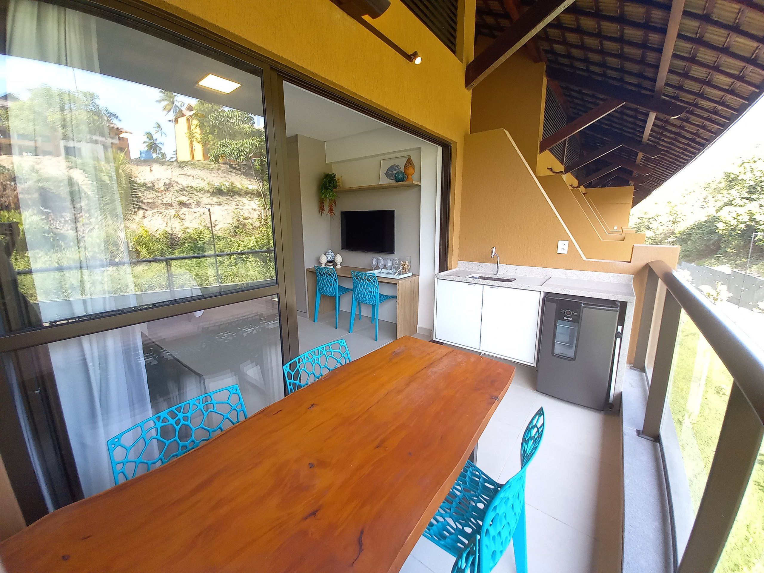 A dining area with a wooden table and blue chairs, a kitchen with a sink and a dishwasher, and a TV mounted on the wall.