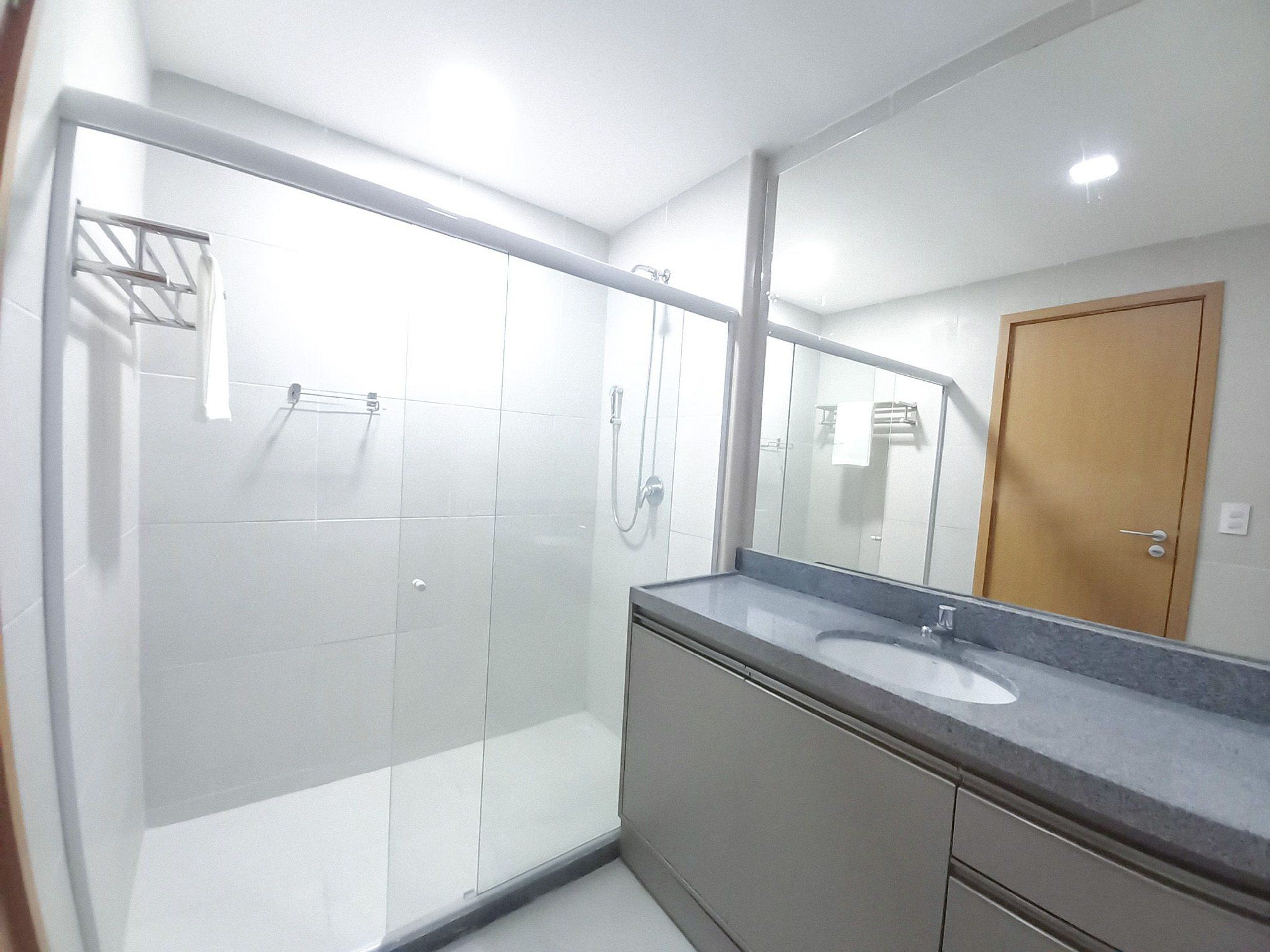 A modern bathroom with a glass shower enclosure, a large mirror, and a sink with a countertop.