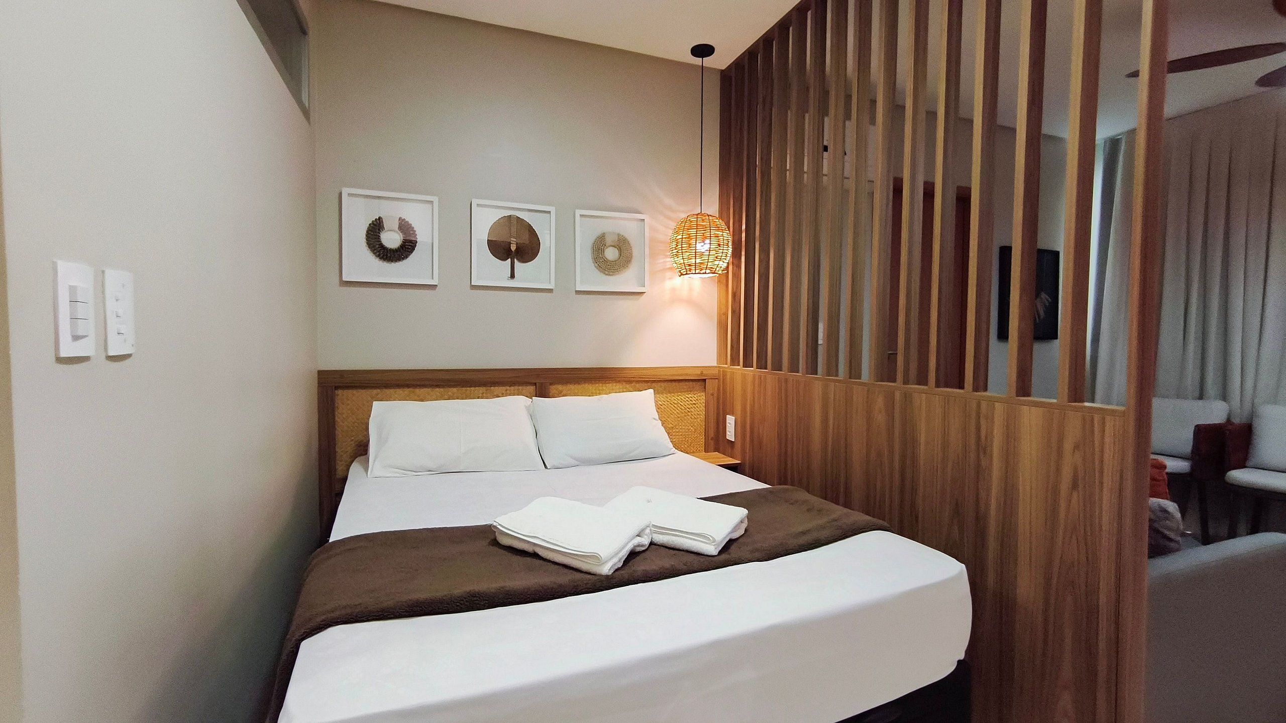 A neatly made bed with white linens, a brown throw blanket, and two folded towels. There are three framed wall decorations above the bed.